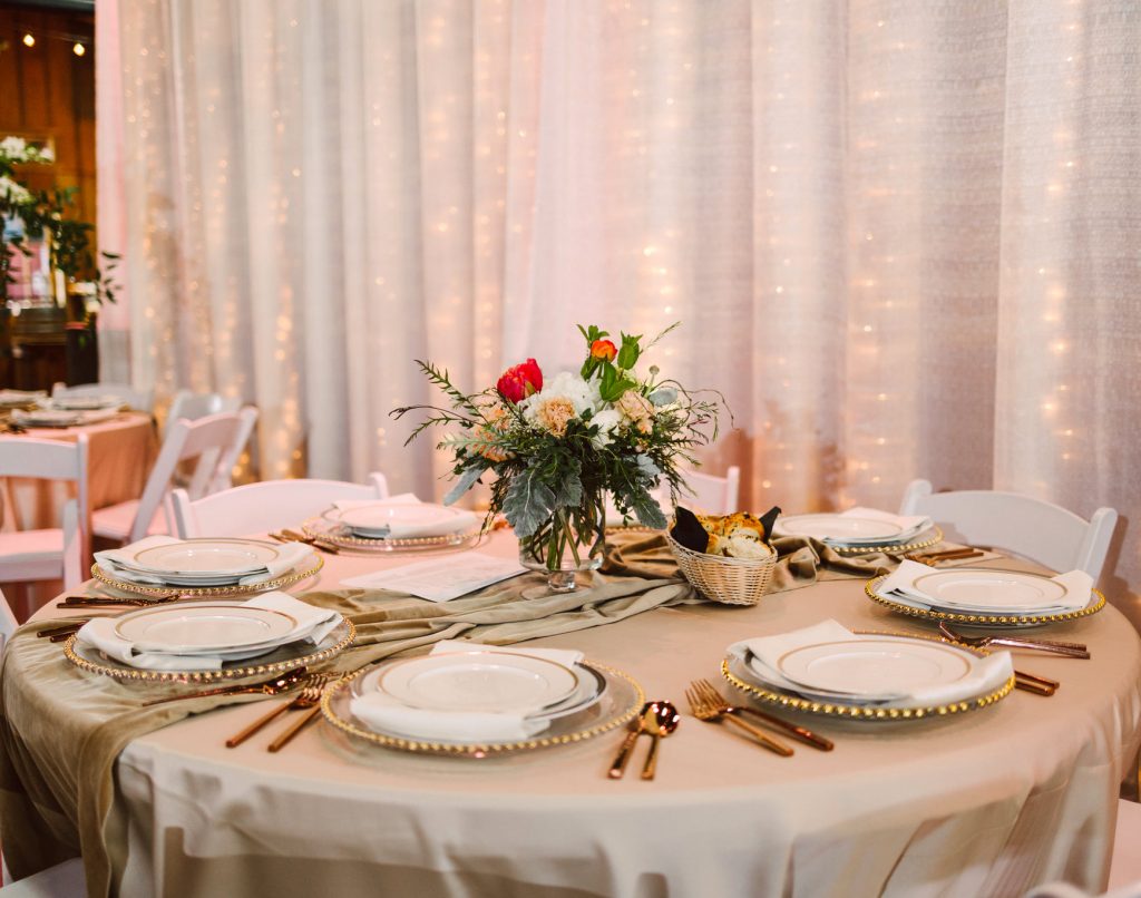 Table set with plates, gold flatware and florals with a linen